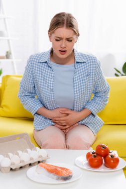 Woman with allergy looking at eggs, tomatoes and salmon on table 