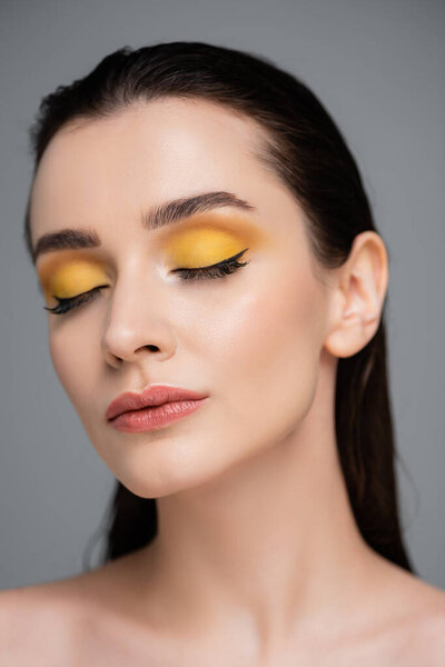 young brunette woman with yellow makeup and closed eyes isolated on grey
