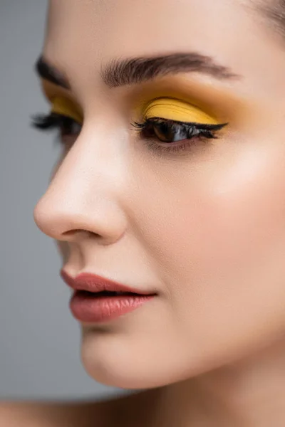 close up of young woman with yellow eyeshadow looking away isolated on grey