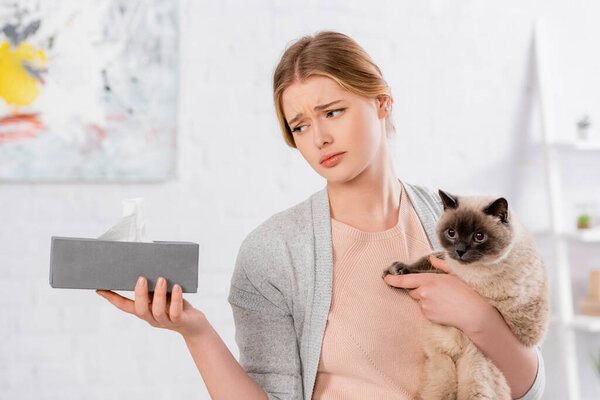 Sad woman holding siamese cat and box with napkin 