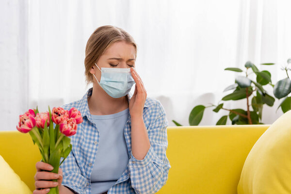 Молодая женщина в медицинской маске держит тюльпаны во время аллергической реакции 