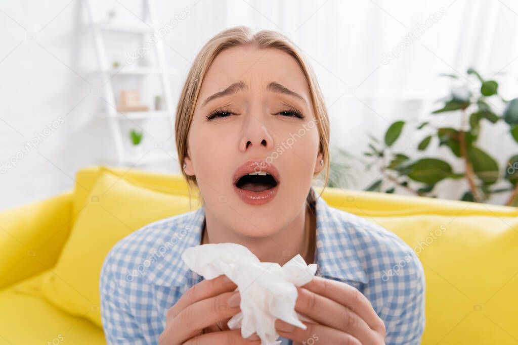 Young woman sneezing and holding napkin on blurred foreground 