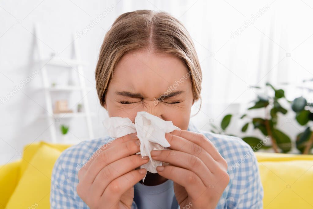 Woman holding napkin near nose during allergy at home 