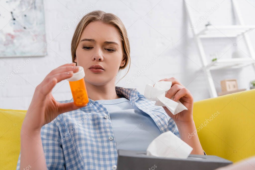 Woman with allergy holding napkin and jar with pills on blurred foreground 