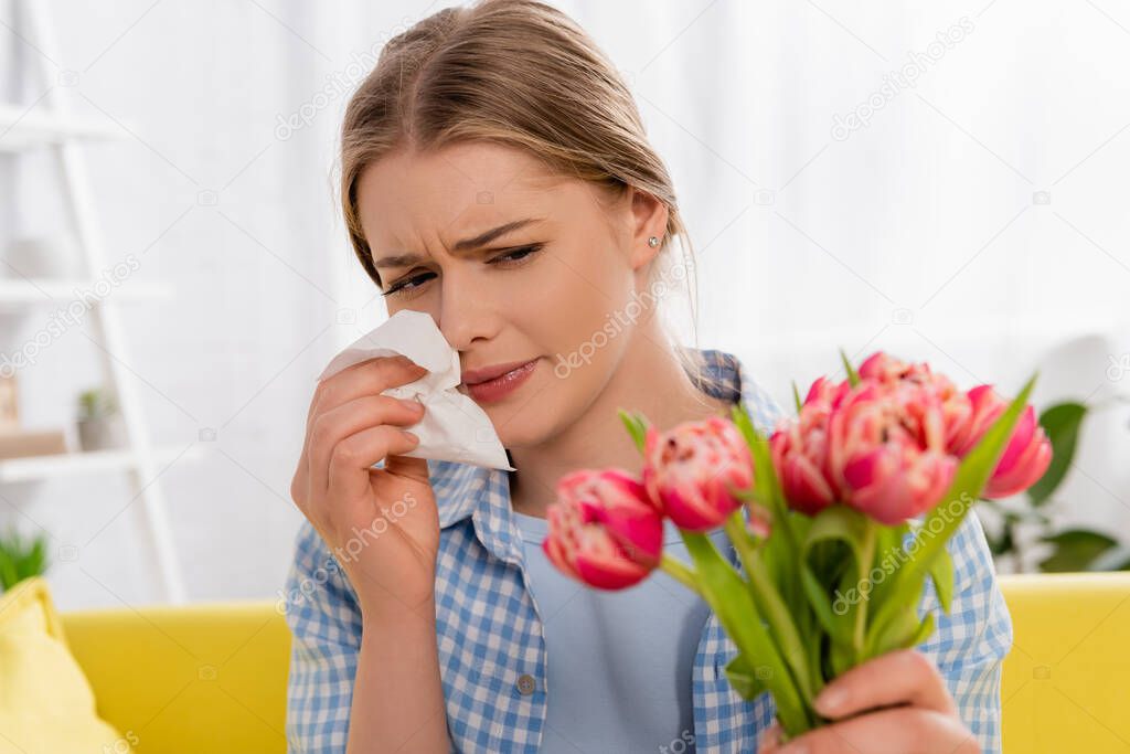 Tired woman holding napkin while suffering from allergy near tulips on blurred foreground 
