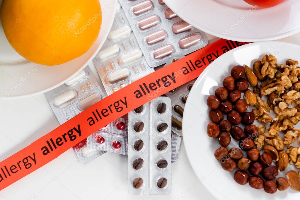 Top view of ribbon with allergy lettering, pills and nuts on table 