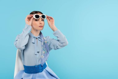 Maviye izole edilmiş kameraya bakarken güneş gözlüğünü çıkaran şık bir kadın.