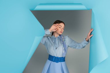 Gri arka planda mavi kağıtta deliğe yakın poz veren zarif bir kadın.