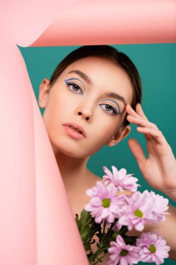 Çiçeklerin yanında yüzüne dokunan büyüleyici bir kadın ve yeşil kağıtta izole edilmiş pembe bir delik.