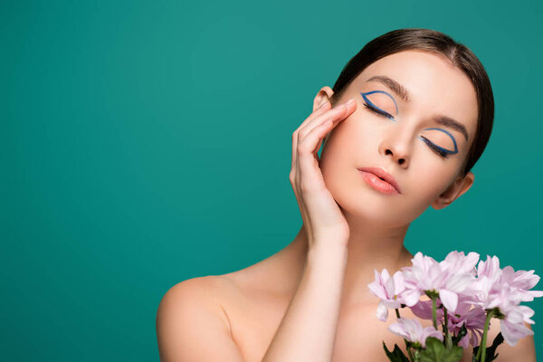young woman with blue eyeliner on closed eyes posing near pink chrysanthemums isolated on green