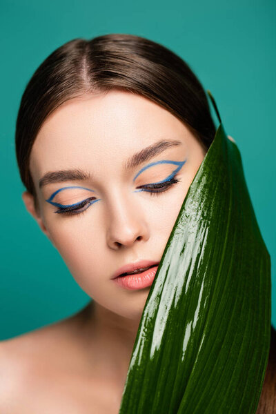 portrait of young woman with blue eyeliner, near shiny leaf isolated on green