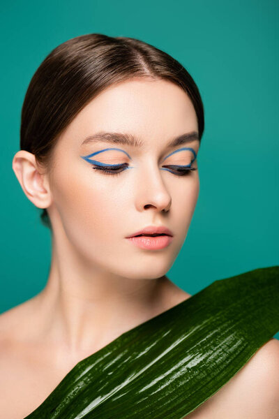 young sensual woman with blue eyeliner near wet leaf isolated on green