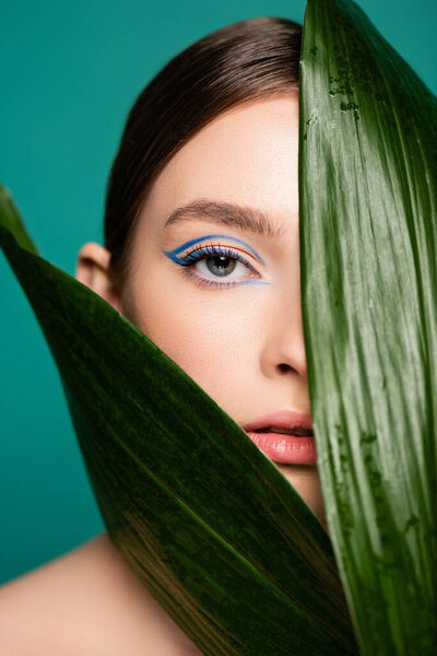 sensual woman looking at camera near glossy leaves isolated on green