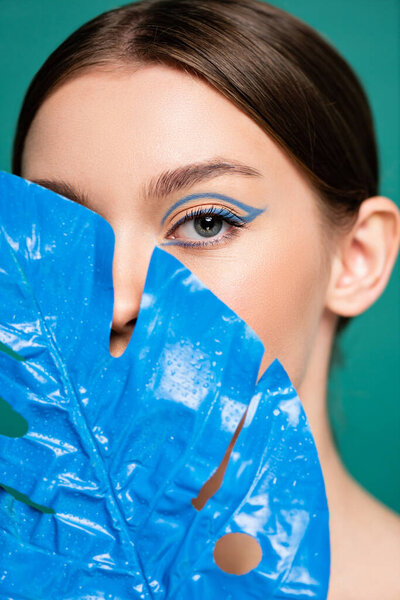 portrait of young woman obscuring face with blue wet leaf isolated on green