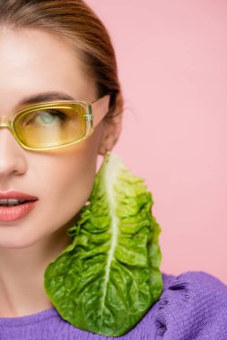 close up view of young woman in colored eyeglasses, with fresh lettuce earring isolated on pink clipart