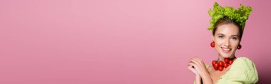 Şapkalı, kolyeli ve pembe pankarttaki sebzelerden yapılmış küpeli çekici bir kadın.