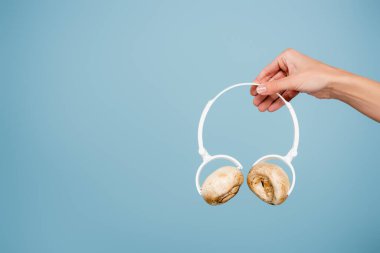 cropped view of woman holding headphones with mushrooms isolated on blue clipart