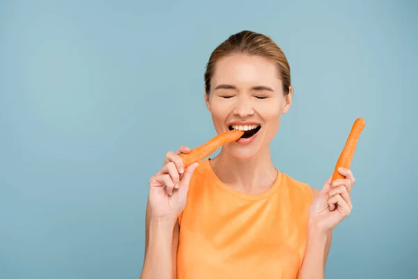 Cheerful Young Woman Closed Eyes Biting Whole Carrot Isolated Blue — Stock Photo, Image