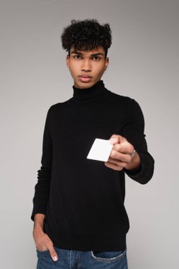 Balıkçı yaka kazaklı genç Afro-Amerikan adam Gri üzerinde boş kart veriyor.