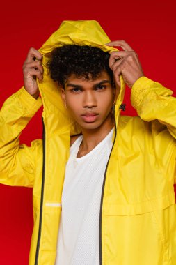 Sarı yağmurluk giymiş şık Afrikalı Amerikalı adam kırmızı başlığı düzeltiyor.