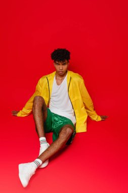 Sarı ceketli, kırmızı üzerinde poz veren, piercing takmış Afro-Amerikan bir adam.