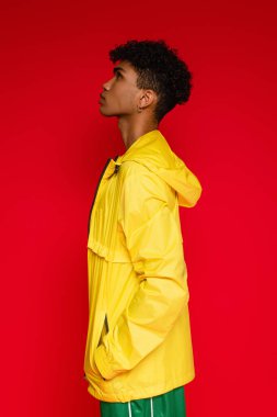 Kırmızı üzerine izole edilmiş sarı ceketli Afro-Amerikan adamın yan görüntüsü.