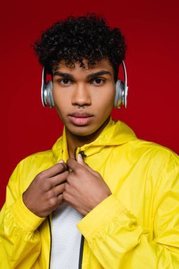 Sarı ceketli Afro-Amerikan adam kırmızıda izole edilmiş kablosuz kulaklıklarla müzik dinliyor.