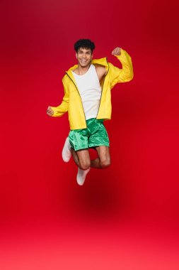 full length of smiling african american man in yellow jacket jumping on red clipart
