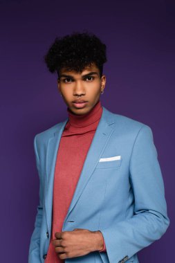 Kıvırcık Afrikalı Amerikalı mavi ceketli adam mor renkli kameraya bakıyor.