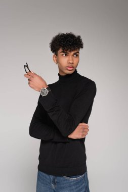 Siyah balıkçı yaka kazaklı genç Afrikalı Amerikalı adam gri gözlüklü poz veriyor.