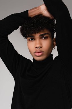 Siyah balıkçı yaka kazak giyen delinmiş Afro-Amerikan adam gri üzerine izole edilmiş poz veriyor.