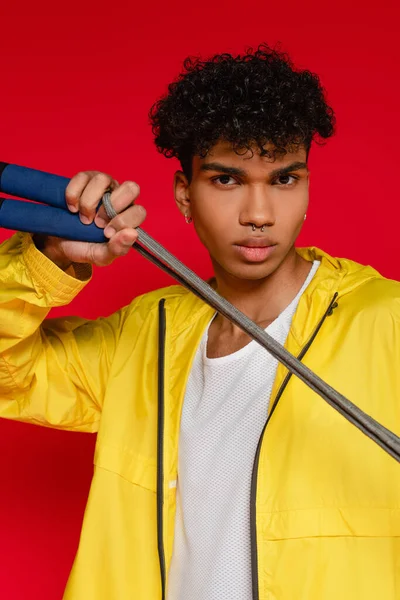 Sarı yağmurluk giymiş delinmiş Afro-Amerikan adam kırmızı üzerinde izole edilmiş ip tutuyor.