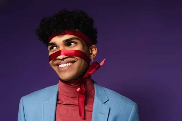 positive african american man tied with red ribbon on purple