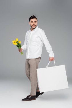 Sarı laleler ve gri arka planda alışveriş çantası tutan gülümseyen adam.