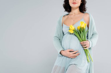 Cropped view of pregnant woman holding bouquet isolated on grey  clipart
