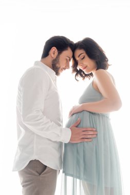 Beyaz elbiseler içinde hamile bir kadının karnına dokunan adamın yan görüntüsü.