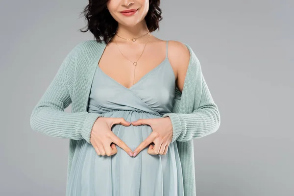 満面の笑みを浮かべて妊娠中の女性は灰色で隔離された腹の近くにハートサインを示す — ストック写真