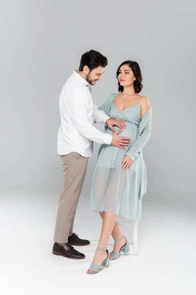 陽気な男持っています手上の妊娠中の妻の腹上の灰色の背景 — ストック写真