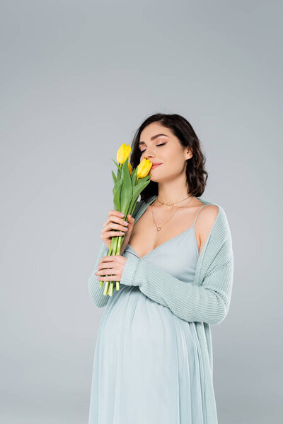 Pretty pregnant woman smelling tulips isolated on grey 