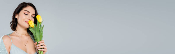 Young woman smelling tulips isolated on grey, banner 