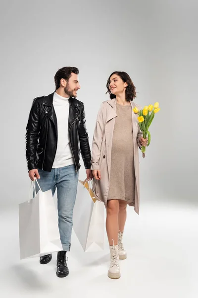 Mujer Embarazada Sonriente Con Flores Caminando Cerca Marido Con Bolsas — Foto de Stock