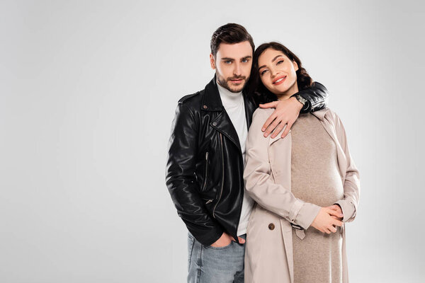 Stylish man hugging smiling pregnant wife isolated on grey 