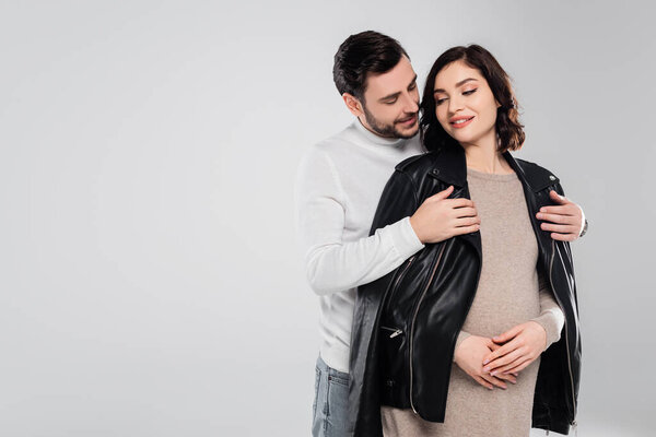 Smiling man wearing jacket on young pregnant wife isolated on grey 