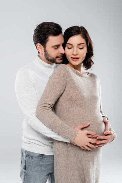 Man hugging pregnant wife in dress isolated on grey 