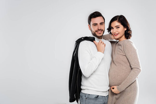 Pregnant woman smiling at camera near husband with leather jacket isolated on grey 