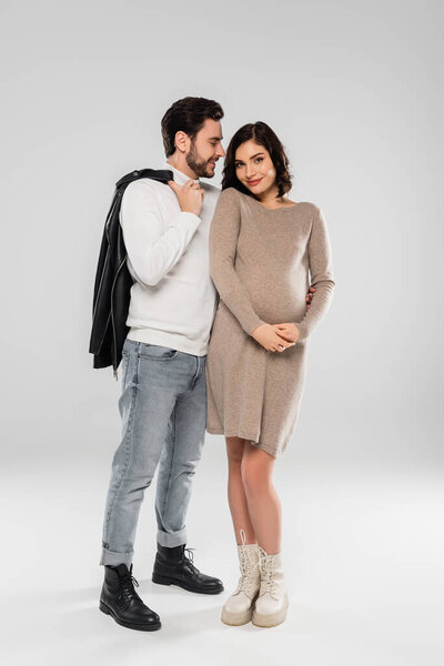 Cheerful man looking at pregnant wife on grey background 