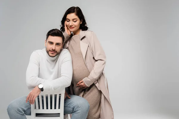 妊娠中の女性でドレスとコート立って近く夫上の椅子に隔離されたグレー — ストック写真