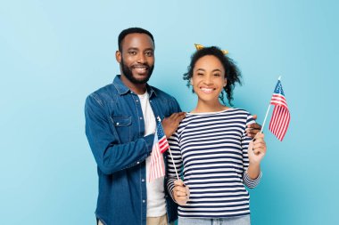 Mutlu Afro-Amerikan çifti, mavi kameraya gülümserken küçük Amerikan bayrakları taşıyor.