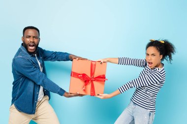 envy african american husband and wife taking away gift box from each other on blue clipart