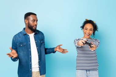 KYIV, UKRAINE - 23 Ekim 2020: Afro-Amerikan adam, mavi üzerine oynayan eşinin yanında omuz silkme hareketi gösteriyor